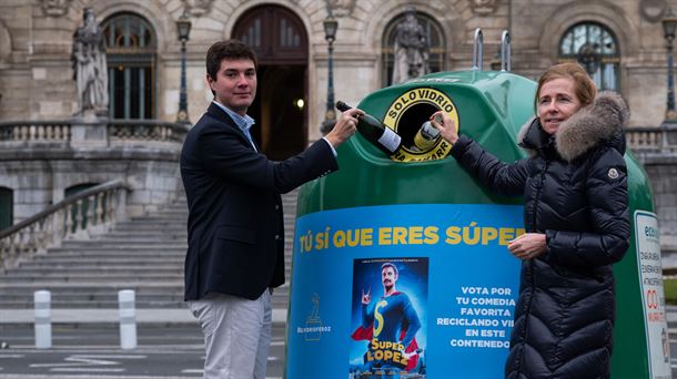 Dos personas depositan botellas de vidrio en un contenedor con el cartel de la película Super López