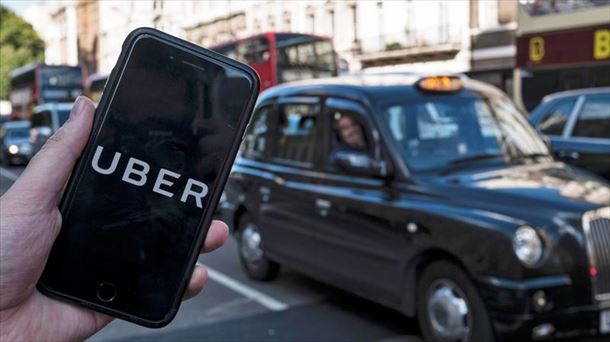 Pertson bat Uber konpainiaren aplikazioarekin, Londreseko taxi baten parean.