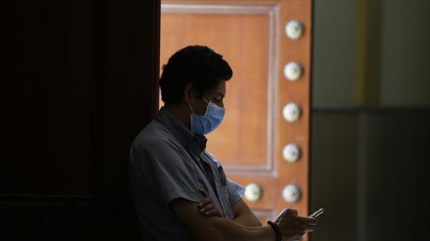 Un hombre observa su teléfono móvil con una mascarilla como medida contra el coronavirus.