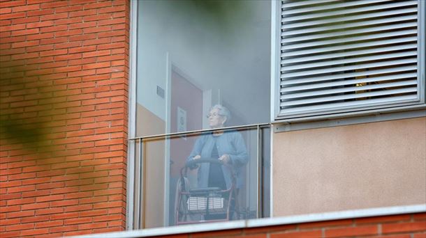 Una mujer mayor mira por la ventana de una residencia.