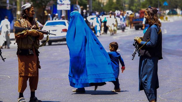 Una mujer cruza la calle en Kabul ante la mirada de dos hombres armados